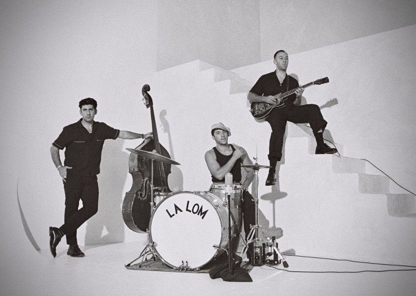 A black and white image of three men dressed in black by a staircase with instrumentsx